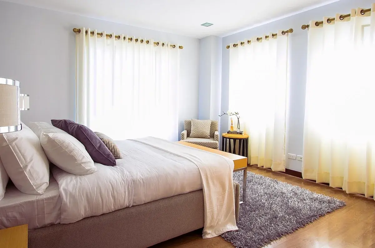 A bright bedroom with a bed, pillows, curtains, and a rug.